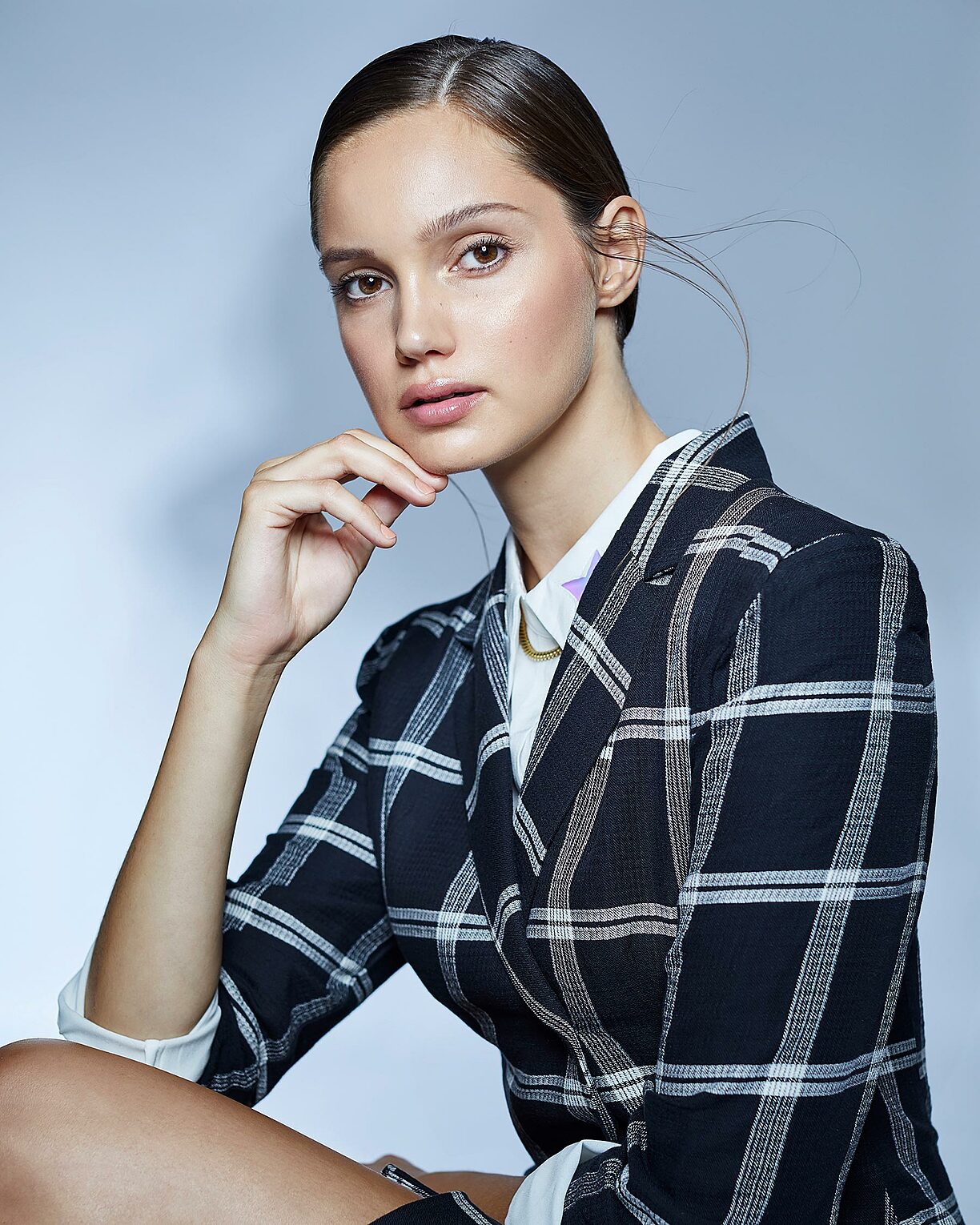 A female model who wears a checked blazer with a white blouse and sleek brown hair