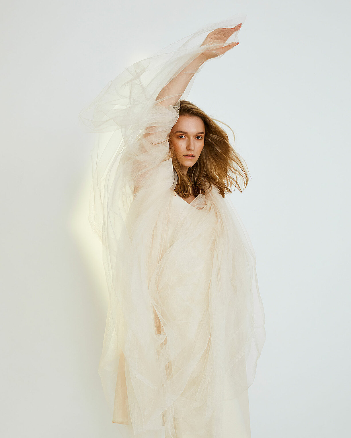 A blonde model in a white/ beuge tull dress with a dynamic movement